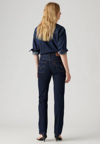 Donkerblauwe denim jeans met een slim fit, voorzien van achterzakken met gebogen naden, gecombineerd met een donkerdenim overhemd en hakken.