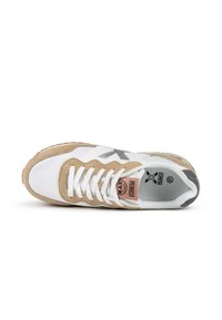 Zapatilla blanca y beige con materiales de ante y cuero, con punta redonda, cordones y una etiqueta de logo en el costado. Suela de goma.
