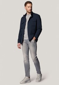 Granatowa kurtka z dwiema kieszeniami na piersi, zestawiona z jasnoszarym swetrem i wyblakłymi szarymi dżinsami. Charakteryzuje się jasnoszarymi sneakersami. Prosty krój.