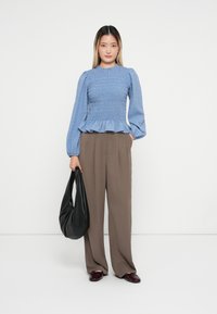 Blå smocket peplum topp med lange ermer, kombinert med løse brune bukser. Tilbehøret inkluderer en svart skulderveske og burgunder sko.