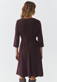 Robe bourgogne à manches trois-quarts, avec une taille cintrée et une jupe évasée. Caractéristiques d'une fermeture éclair au dos et d'un tissu doux et texturé.