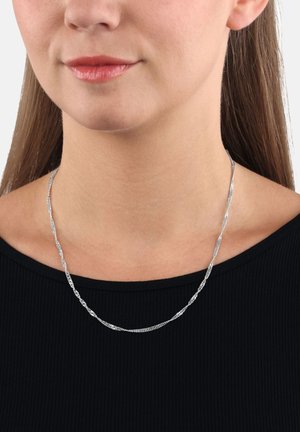 La collana in argento presenta un intricato design attorcigliato, poggiata su un collo nudo, indossata su un top a coste nero.