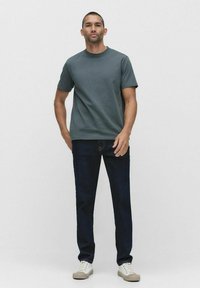 Grå bomullströja, rund hals, korta ärmar, i kombination med mörkblå jeans. Modellen bär vita sneakers med ljusbruna sulor. Enkelt design.