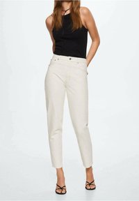 Jean taille haute beige clair avec une coupe droite, poches avant et fermeture éclair. Accompagné d'un haut sans manches noir et de sandales à lanières.