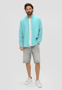 Türkisfarbendes Langarmhemd, weißes Rundhals-T-Shirt, graue Shorts und weiße Sneaker. Lässiger, lockerer Schnitt, Knopfverschluss-Design und minimalistischer Stil.