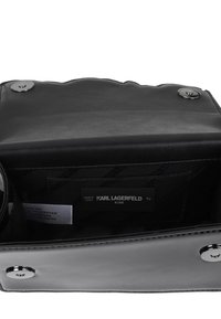 Sac à main en cuir noir avec une texture brillante, présentant une fermeture à pression magnétique, une étiquette intérieure et un compartiment de rangement.