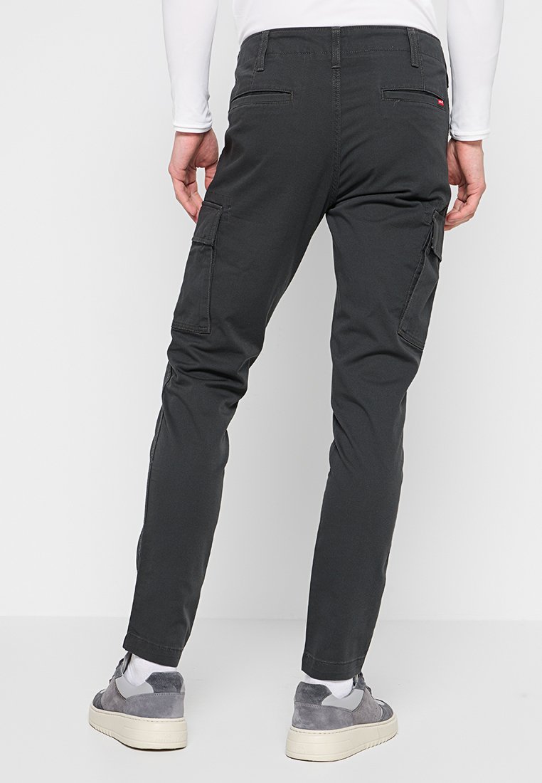 Pantalones cargo gris oscuro con un ajuste slim, que presentan bolsillos laterales, una textura suave y costuras reforzadas. Llevados con zapatillas grises.