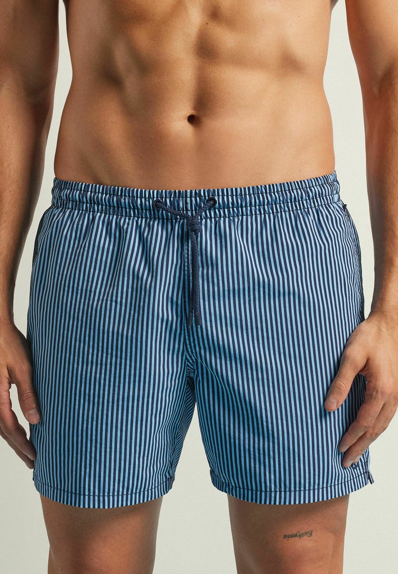 Bañador a rayas azul y blanco, hecho de un tejido ligero, que cuenta con una cintura elástica con cordón y bolsillos laterales.