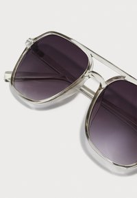 Occhiali da sole con una montatura trasparente, grandi lenti scure e un design elegante. Notabili per la loro forma angolare e gli accenti hardware minimi.