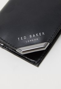 Fekete bőr pénztárca ezüst színű fémszegéllyel, reliefbélyegzett "TED BAKER" és "LONDON" felirattal, rendezett varrással az éleken.