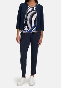 Navy jacket with a textured finish, patterned top in black, white, and blue, paired with navy pants and white sneakers.