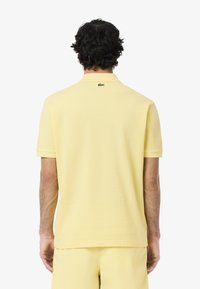 Polo shirt giallo Lacoste con maniche corte e colletto classico, con logo verde del marchio sul retro. Tessuto liscio, vestibilità regolare.