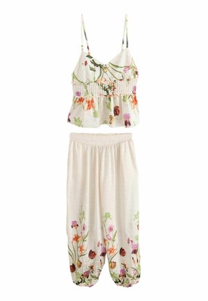 Nahaufnahme eines hellbeigen Rocks mit großen Punkten und einem floralen Oberteil, das hochgehoben ist, um einen nackten Bauch und Bauchnabel zu zeigen.