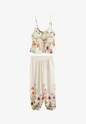 Nahaufnahme eines hellbeigen Rocks mit großen Punkten und einem floralen Oberteil, das hochgehoben ist, um einen nackten Bauch und Bauchnabel zu zeigen.