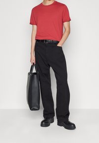 Camiseta de algodón roja, corte holgado; pantalones negros de cintura alta; bolso de tote negro de cuero; zapatos gruesos negros; diseño minimalista y contraste de colores.