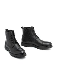 Botas de cuero negro hasta el tobillo con puntera redondeada, cordones en la parte frontal, cremallera lateral y suelas resistentes para un mejor agarre. Textura suave con un detalle de costura sutil.