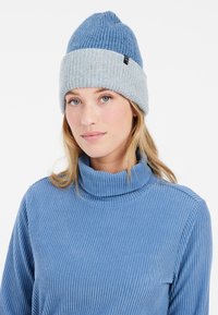 Blau gestrickte Mütze mit einem hellblauen umgeschlagenen Bund und strukturiertem Muster, getragen mit einem passenden gerippten Rollkragensweater.