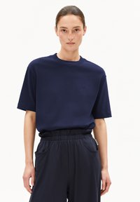 Navyblauwe katoenen t-shirt met korte mouwen, ronde hals en subtiel geborduurd logo op de borst. Gepaarde met donkergekleurde elastische taillebandbroek.