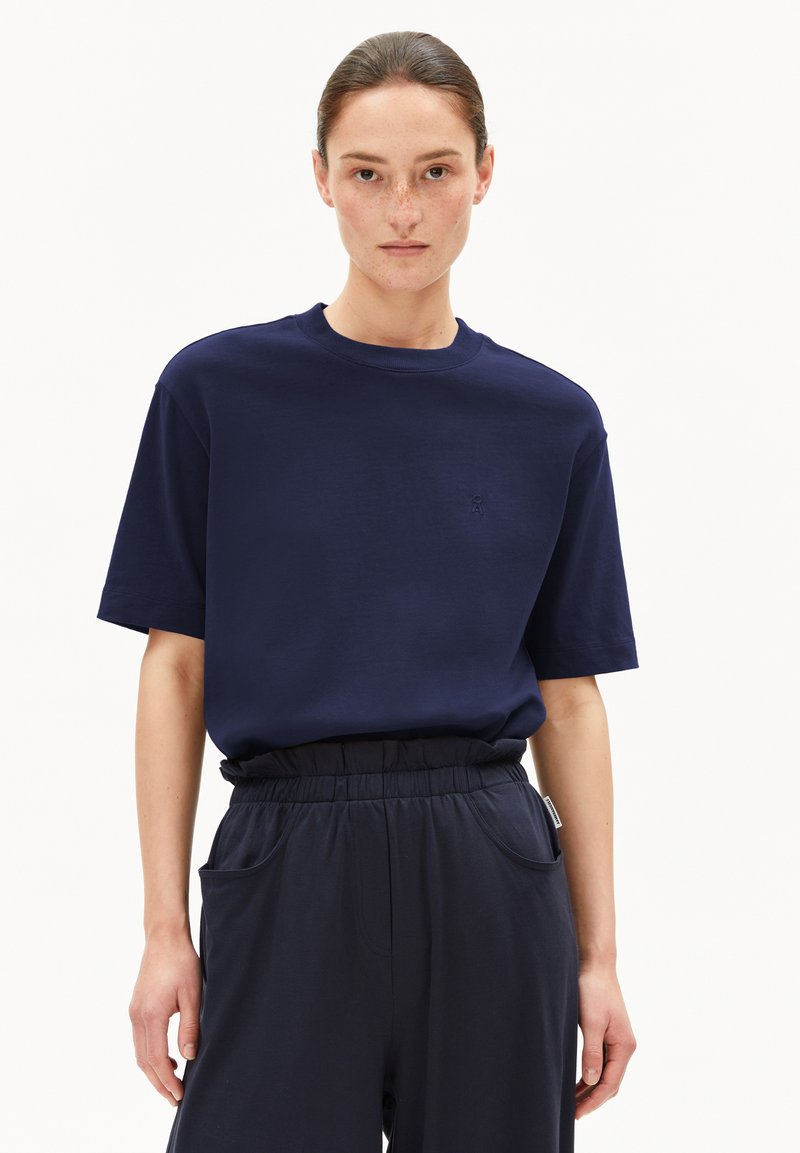 Navyblauwe katoenen t-shirt met korte mouwen, ronde hals en subtiel geborduurd logo op de borst. Gepaarde met donkergekleurde elastische taillebandbroek.