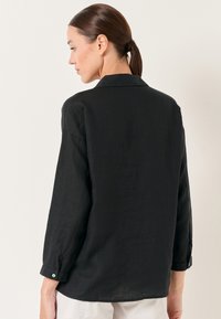 Camicia nera di lino con maniche lunghe, colletto e polsini abbottonati. Presenta una vestibilità comoda e una texture sottile. Vista posteriore mostrata.