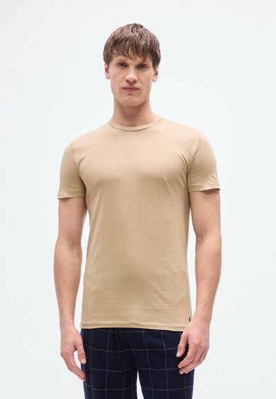 Μπεζ εφαρμοστό κοντομάνικο μπλουζάκι με στρογγυλή λαιμόκοψη, κατασκευασμένο από απαλό ύφασμα. Σημαντικές λεπτομέρειες περιλαμβάνουν ομαλή υφή και ελάχιστες ραφές.