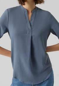 Haut bleu à manches courtes avec un col cranté, fabriqué dans un tissu texturé, présentant un drapé subtil et une coupe décontractée.