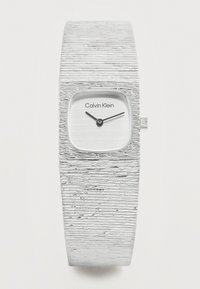 Ασημένιο ρολόι χειρός Calvin Klein με υφασμένο φαρδύ λουράκι και μικρό τετράγωνο καντράν που δείχνει ώρα 10:10.