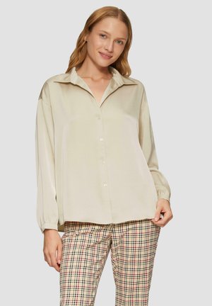 Cream-colored button-up blouse with a soft texture, long sleeves, and a classic collar, paired with plaid patterned trousers.