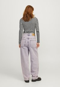 Lilafargede høy midje baggy jeans har en teksturert overflate, fem lommer og en brun lærlabel på baklommen. Stripete langermet topp er synlig.