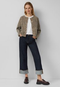 Jas met luipaardprint in beige en bruin tinten, ronde halslijn en drie knopen, gecombineerd met donkere wijde jeans en zwarte loafers.