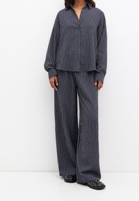 Ensemble en deux pièces rayé bleu marine en tissu doux. Comprend une chemise à bouton avec des manches larges et un pantalon long ample.