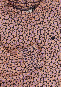 Luipaardprint-blouse met een geplooide halslijn en elastische manchetten. De stof is een mix van oranje en lavendel op een donkere achtergrond.