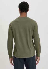 Langarmshirt aus olivgrüner Baumwolle. Hat einen Rundhalsausschnitt, gerippte Bündchen und seitliche Schlitze am Saum für zusätzlichen Komfort. Einfaches Design.