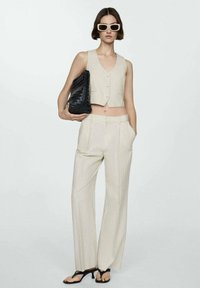 Beige striped cropped vest with buttons, matching high-waisted pants, and black woven shoulder bag. Accented with black strappy sandals.