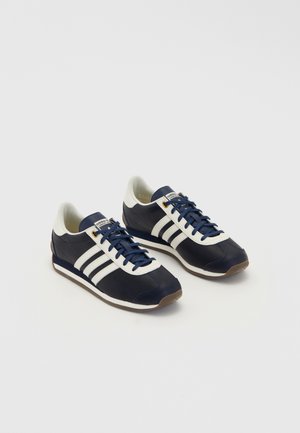 Paire de baskets Adidas bleu marine et blanc avec des lacets bleus et trois bandes blanches de chaque côté, présentée sur un fond blanc uni.