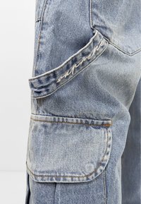 Hellblaue Denim-Cargohosen mit einer großen Seitentasche, gesticktem "Supreme"-Label, sichtbaren Nähten und einer lässigen Passform.