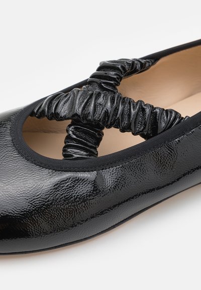 Zwarte patenten ballerina met een gestructureerd oppervlak, voorzien van een gerimpeld zwart elastisch kruisdetail en een ronde neus.