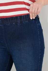 Ručně tahání za elastický pás tmavě modrých džín, které jsou oblečené s červeno-bílým pruhovaným tričkem, ukazujícím texturu látky a střih.