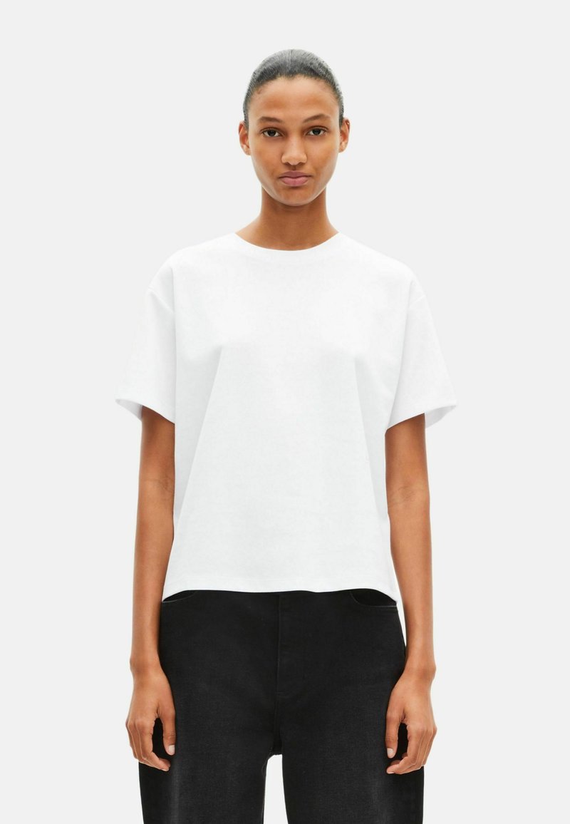 Camiseta blanca de manga corta con cuello redondo y corte holgado, confeccionada en tela suave. Combinada con pantalones negros de tiro alto.