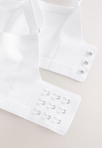 Gros plan sur la fermeture dos d'un soutien-gorge blanc avec trois rangées de crochets et d'yeux pour un réglage ajustable sur une surface claire.