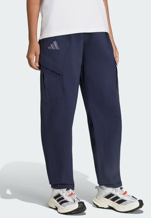 Marineblå cargobukser med sidelommer, båret med hvide og sorte Adidas-sneakers med orange detaljer og en hvid skjorte.