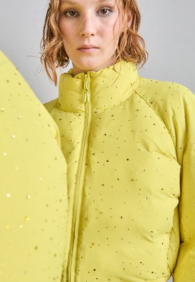 Yellow padded jacket featuring a high collar, full zip closure, and embellishments of small metallic dots scattered across the surface.