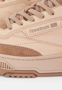 Beige Reebok sneakers featuring a smooth leather upper with suede accents, textured laces, and a rubber sole with defined tread patterns.