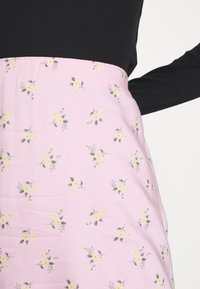 Roze bloemenrok met kleine gele bloemen en groene bladeren op een lichtgewicht stof, voorzien van een elastische tailleband. Zichtbare zwarte lange mouwen top.