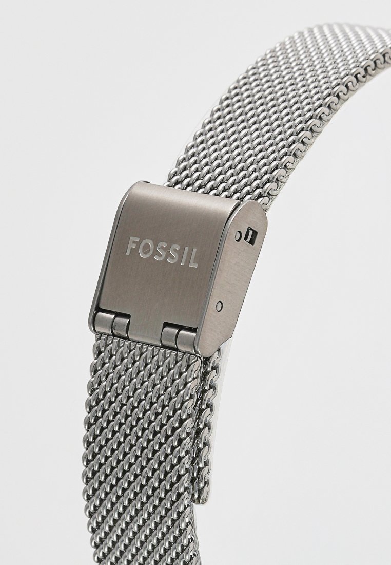 Srebrny pasek do zegarka z siatki, wykonany ze stali nierdzewnej, z metalowym zapięciem z wygrawerowanym napisem "FOSSIL", prezentujący elegancką tkaną strukturę.