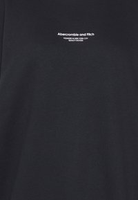 Tessuto nero con testo bianco "Abercrombie and Fitch Fondata a New York City Merce di Qualità" centrato vicino alla parte superiore.