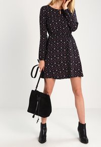 Svart blommig klänning med långärmar, elastisk midja och nyckelhalsringning. I kombination med en svart suéde bucket-väska och svarta ankelstövlar.