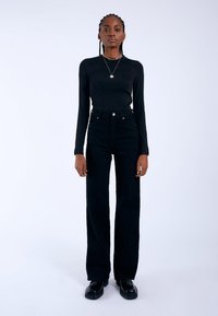 Black long-sleeve top paired with high-waisted black jeans. The outfit features a fitted design, smooth texture, and minimal hardware accents.