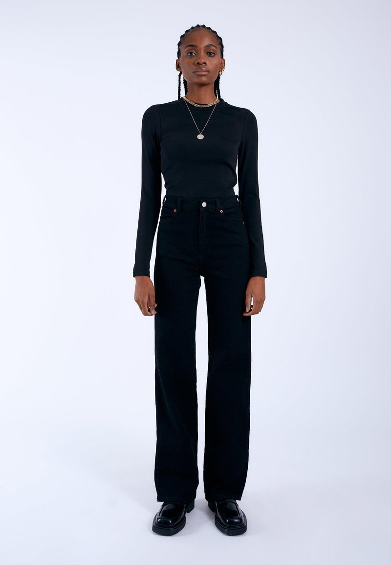 Black long-sleeve top paired with high-waisted black jeans. The outfit features a fitted design, smooth texture, and minimal hardware accents.