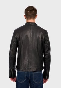 Chaqueta de cuero negro con un corte ajustado, que presenta un alto collar, mangas con cremallera y una textura suave, vista desde la parte de atrás.